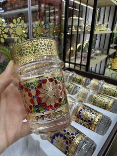 a person holding up a glass in front of many different colored items on display at a store