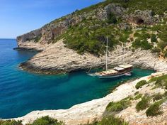 a sailboat is anchored in the blue water near a rocky cliff and shore line