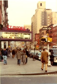 an old photo of people walking on the sidewalk in front of a movie theater sign