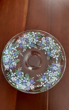 a glass bowl with blue and white flowers painted on the side sitting on a wooden table