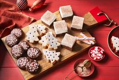 a wooden cutting board topped with cut up cookies and other holiday treats next to a bowl of candy canes