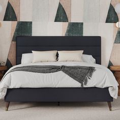 a bed with pillows and blankets on it in front of a wallpapered background