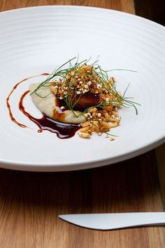 a white plate topped with food on top of a wooden table next to a knife