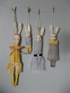 three dolls hanging from clothes pins on a line next to a wall with other doll heads