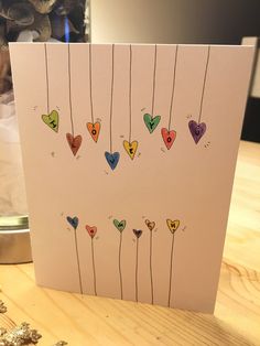 a card with hearts hanging from strings on a table next to a vase filled with flowers