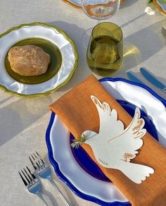 a place setting with an orange napkin and white dove on it, surrounded by silverware