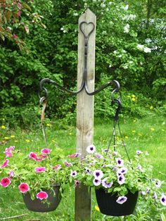 two hanging flower pots with flowers in them on a pole next to some grass and trees