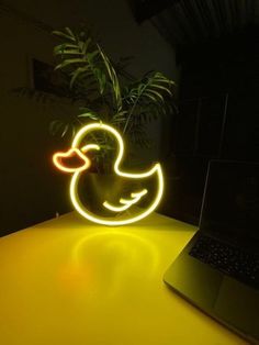 a laptop computer sitting on top of a table next to a neon ducky light