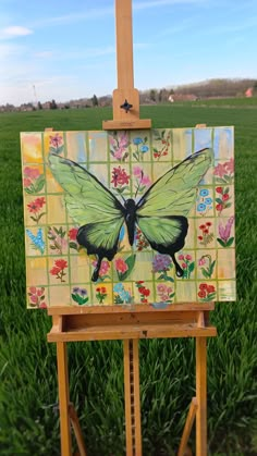 an easel with a painting of a butterfly on it's side in the grass