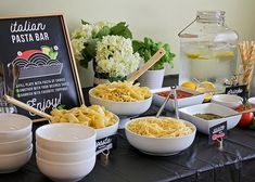 a table topped with bowls filled with pasta and veggies next to a chalkboard sign