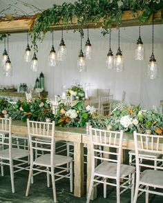 a long table with white chairs and greenery hanging from the ceiling