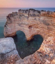 an aerial view of the ocean and cliffs at sunset, with a rock formation in the foreground