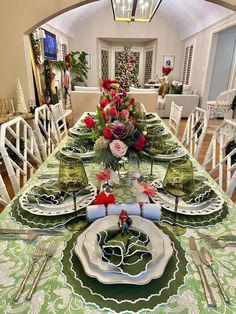 the table is set for christmas dinner with green and white place mats, silverware, and flowers