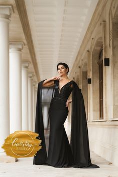 a woman in a black evening gown posing for the camera with her cape draped over her shoulders