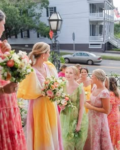 a group of women standing next to each other in front of a white building and holding bouquets