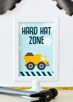 a party zone sign with construction vehicles on it and scissors next to it, in front of a white wall