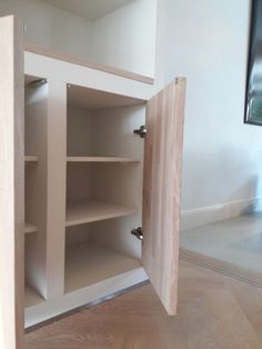 an open cabinet in the corner of a room with hard wood floors and white walls