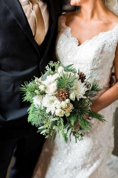 a bride and groom pose for a wedding photo in their tuxedo suit with pine cones on his lapel