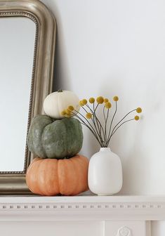 a mirror, vase with flowers and pumpkins on a mantle