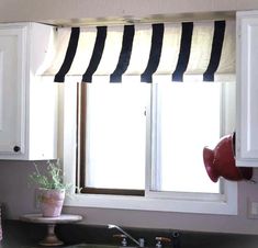 a kitchen window with black and white striped valances on the windowsill, next to a potted plant