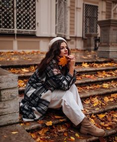 a woman is sitting on the steps and holding an autumn leaf