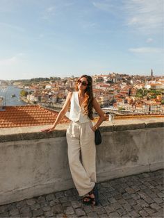 a woman standing on top of a stone wall next to a cityscape with buildings in the background