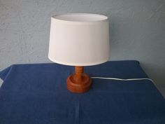 a table lamp with a white shade on it sitting on a blue blanket next to a gray wall