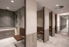 the interior of a modern bathroom with wood benches and mirrors on the wall, along with tile flooring