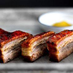 three pieces of meat sitting on top of a counter next to a bowl of sauce