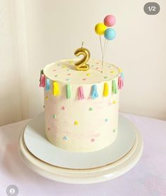 a birthday cake with the number two on top and balloons in the air above it