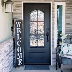 a welcome sign is on the front door of a house with a bench and chair