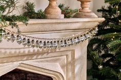 a christmas tree is next to a fireplace with ornaments on it and a garland hanging from the mantel