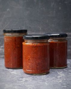 three jars filled with red sauce sitting on top of a gray countertop next to each other