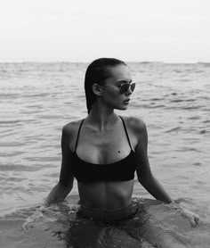 a woman sitting in the water wearing sunglasses