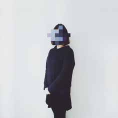 a person standing in front of a white wall wearing a black sweater with squares on it