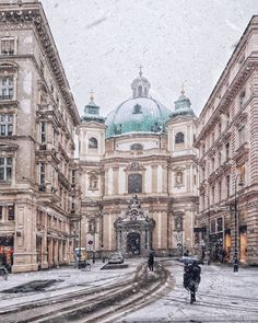 people are walking down the street in front of buildings on a snowy day with snow falling