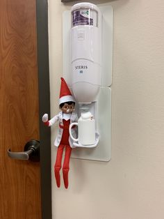 an elf is hanging on the wall next to a water dispenser and cup