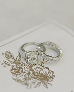 two wedding rings sitting on top of each other next to a card with the word love written on it