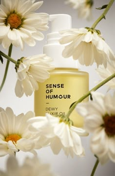 a close up of a bottle of perfume surrounded by white daisies on a table