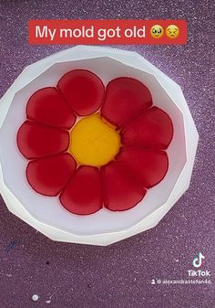 a white bowl filled with red flowers sitting on top of a purple table next to an orange and yellow object