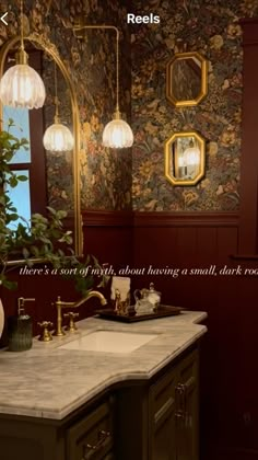 the bathroom is decorated in rich colors and features wallpaper, marble countertops, brass fixtures, and gold accents