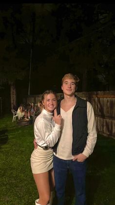 a man standing next to a woman on top of a lush green field at night