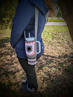 a woman is holding a coffee mug in her hand while wearing a crocheted bag