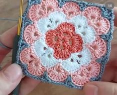 someone is holding a crocheted square with a flower on it and a pencil in their hand