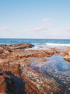 people are swimming in the ocean near some rocks and water on a sunny day with clear blue skies