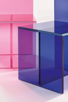 three different colored glass tables on a white floor with pink and blue walls in the background