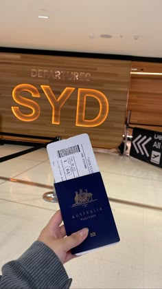 a person holding up a passport in front of a sign that says departure syd