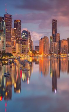 the city skyline is lit up at night, with boats in the water and skyscrapers reflected in the water