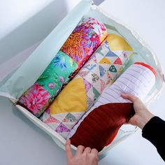 a person is opening an open suitcase filled with colorful pillows and fabric material, while another hand reaches for the pillow