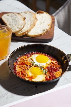 an iron skillet with eggs in it and bread on the table next to it